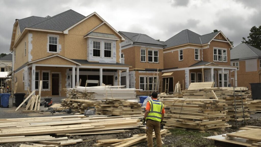 Unfinished houses and construction equipment under a cloudy sky.