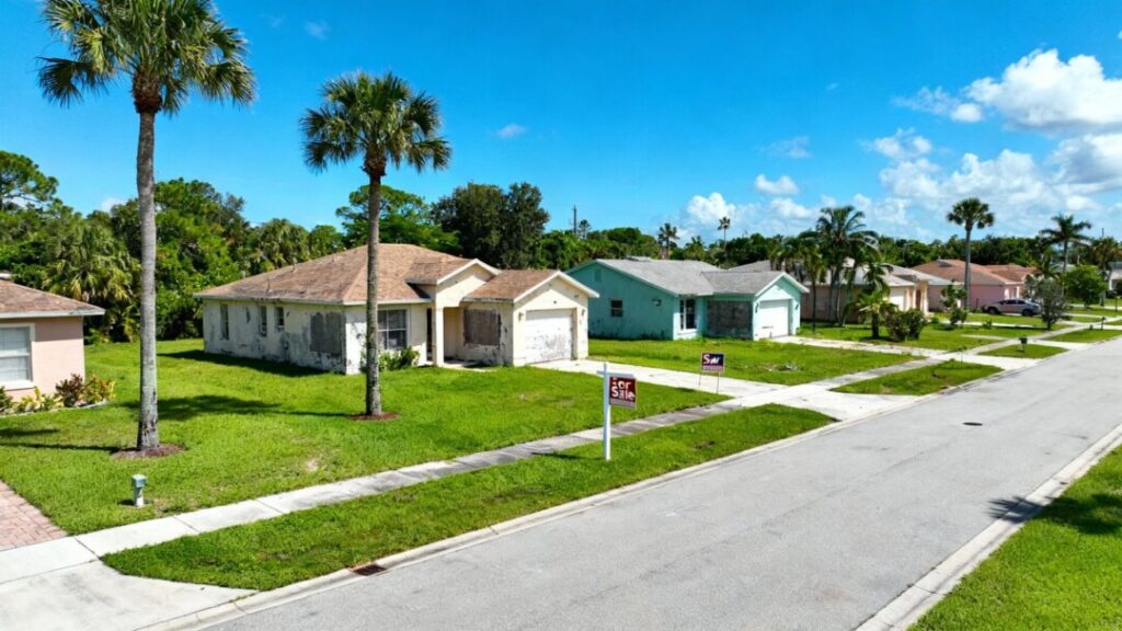 Florida neighborhood homes with for sale signs and palm trees.