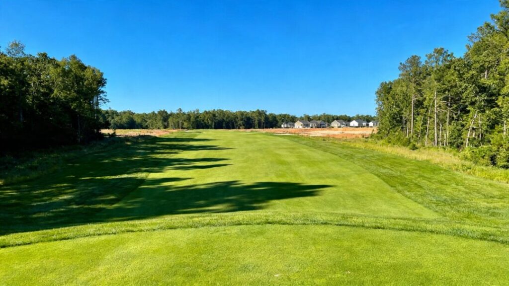 Golf course with houses nearby under a blue sky.